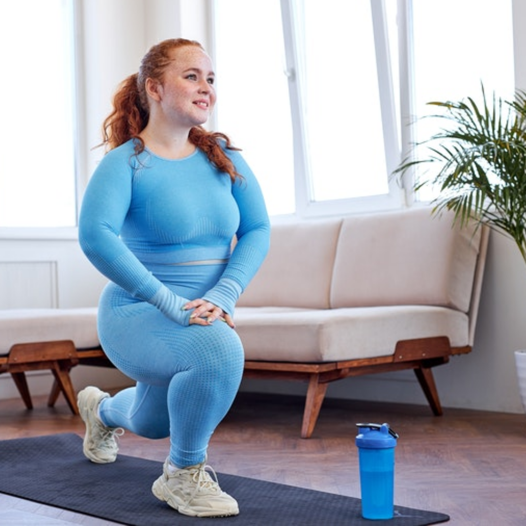 Overweight woman doing stretching exercise for legs at home, doing lunges, redhead caucasian lady in beautiful blue sportswear in bright living room at home, on fitness mat. sport concept