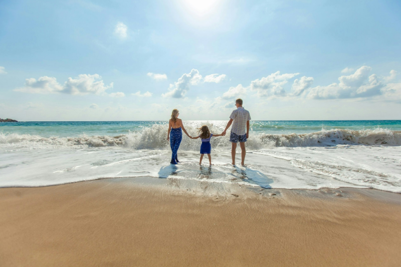 Family of three on beach with blue sky facing sea